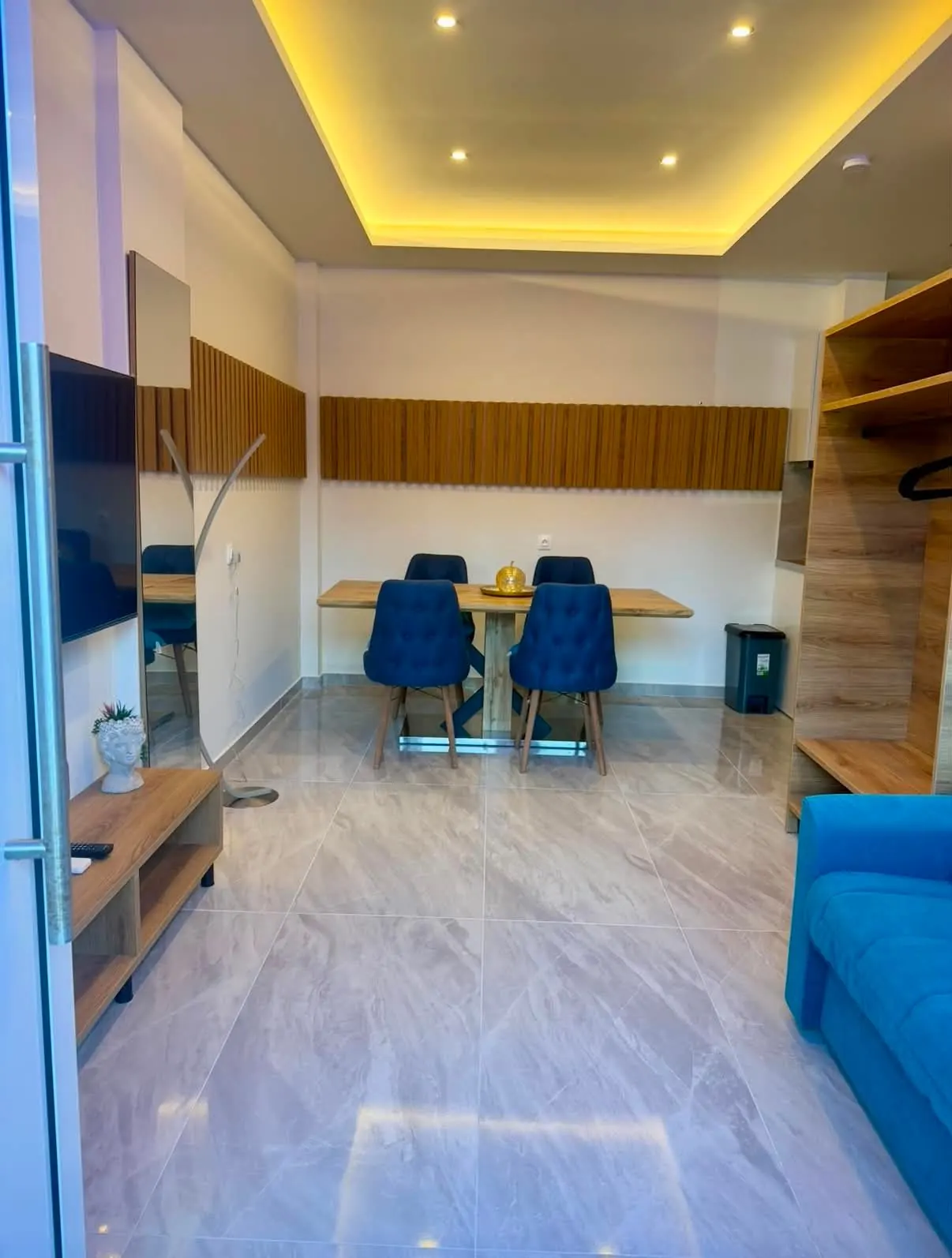 Az 51-es apartman nappali–étkezője tévével, kék kanapéval és négyszemélyes asztallal