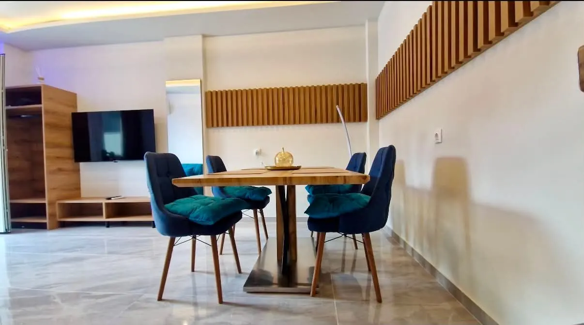 Az 51-es apartman tágas nappalija étkezőasztallal, bársonyszékekkel és fali tévével
